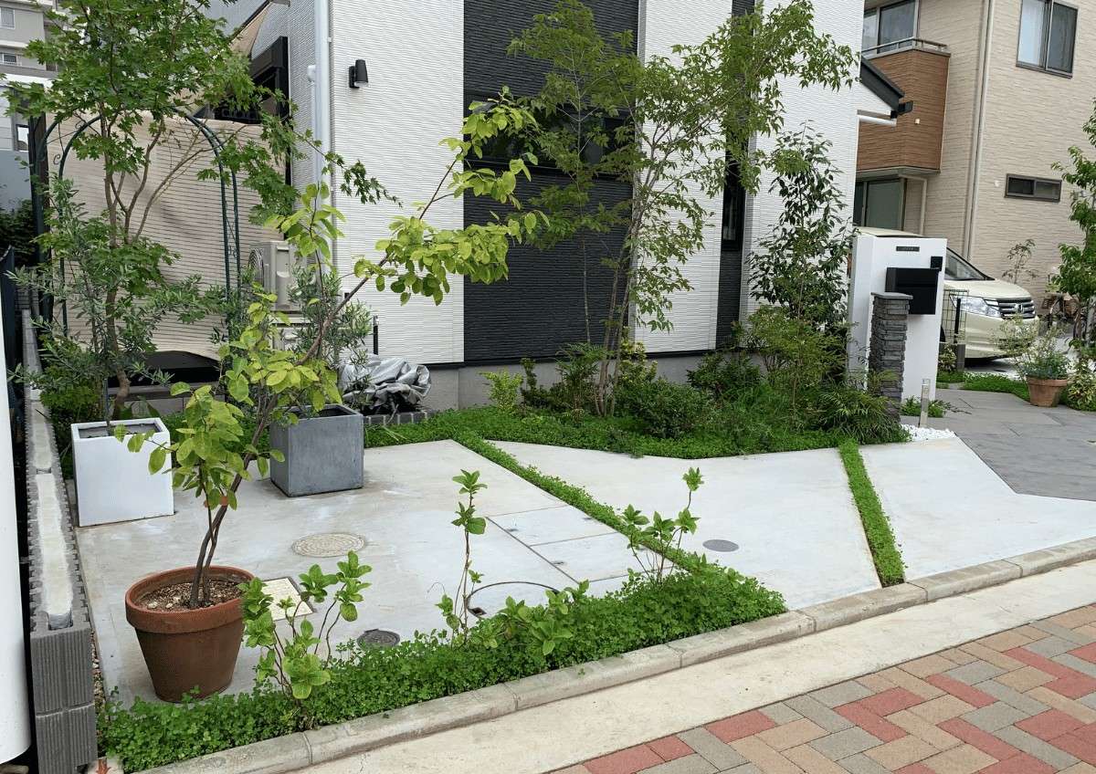 自然石調の敷材と植栽が調和した玄関アプローチの全景。開放感のあるセミクローズ外構。
