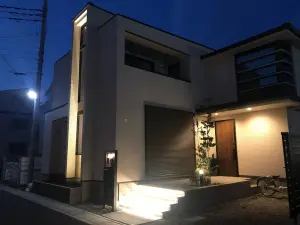 玄関とリビングが入隅になった庭部分がおしゃれなタイルテラスでつなげられ、植栽とともにライトアップされているおしゃれな外構