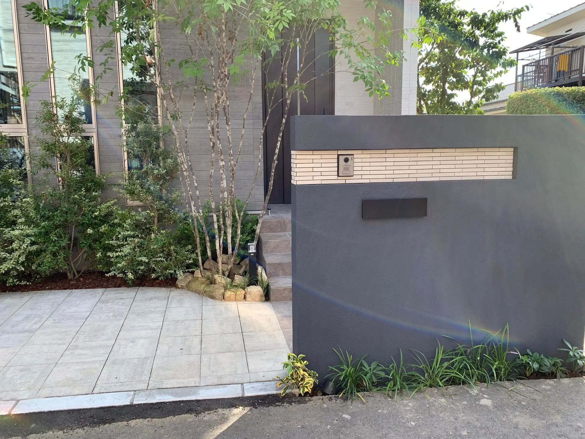 グレーのモダンで大きな門塀とおしゃれな床タイル、植栽がきれいな新築オープン外構の玄関前