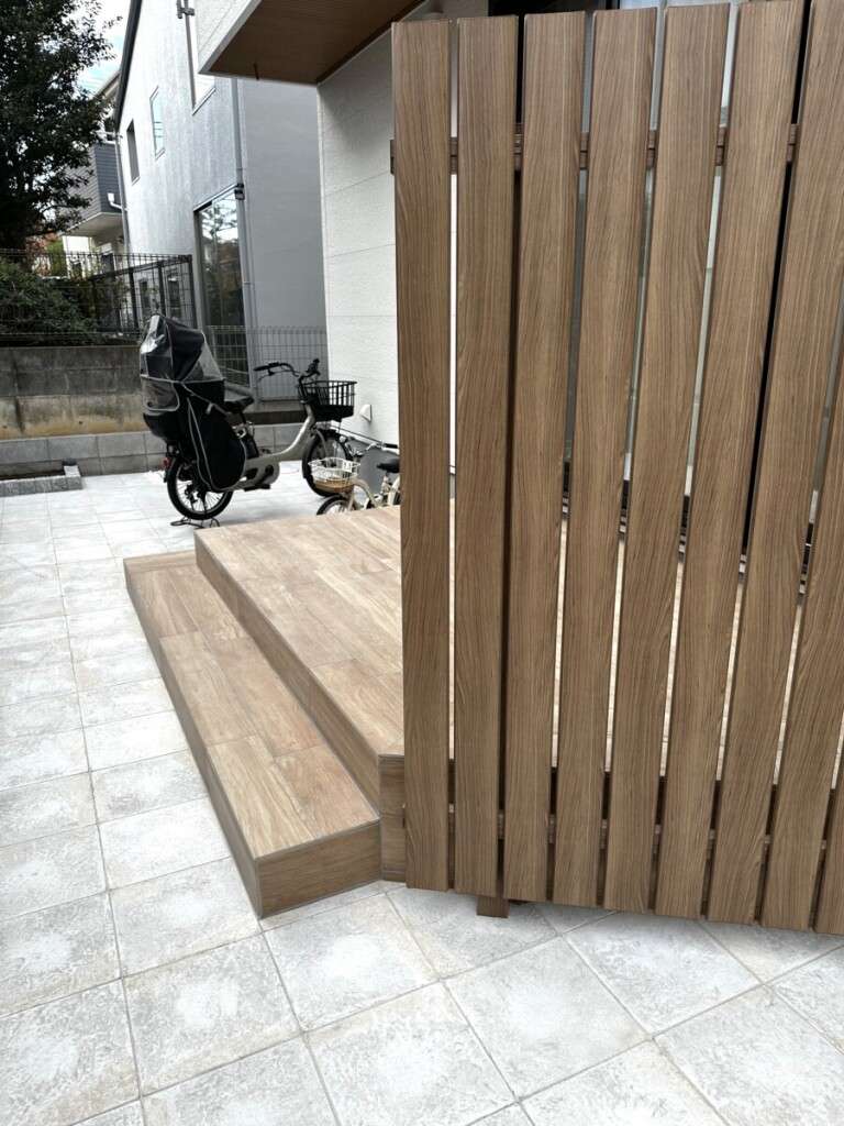 リビング前に設置された木目調タイルデッキ(リビエラ アルピ)と、斜めに配置された目隠しフェンス
