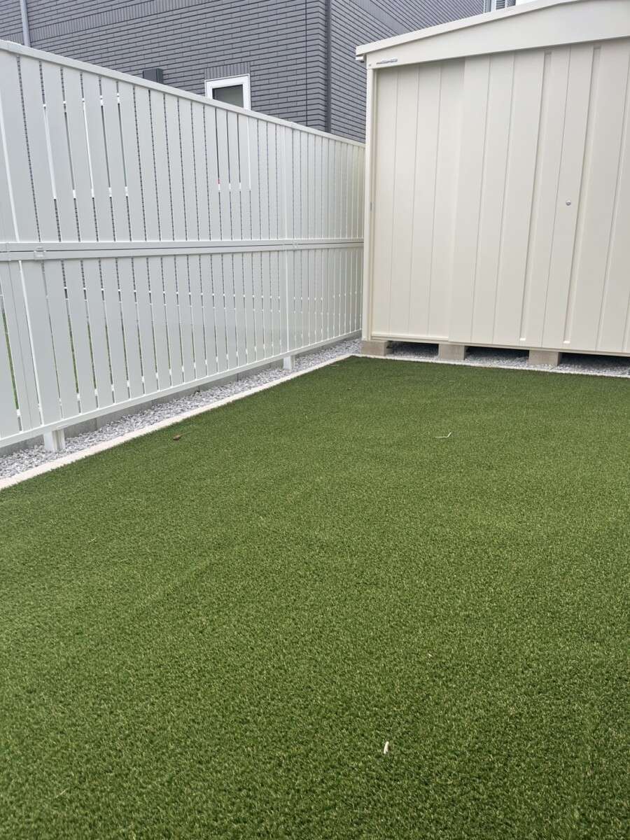 北欧風のやさしい雰囲気が広がる物置と人工芝、目隠しフェンスのある庭