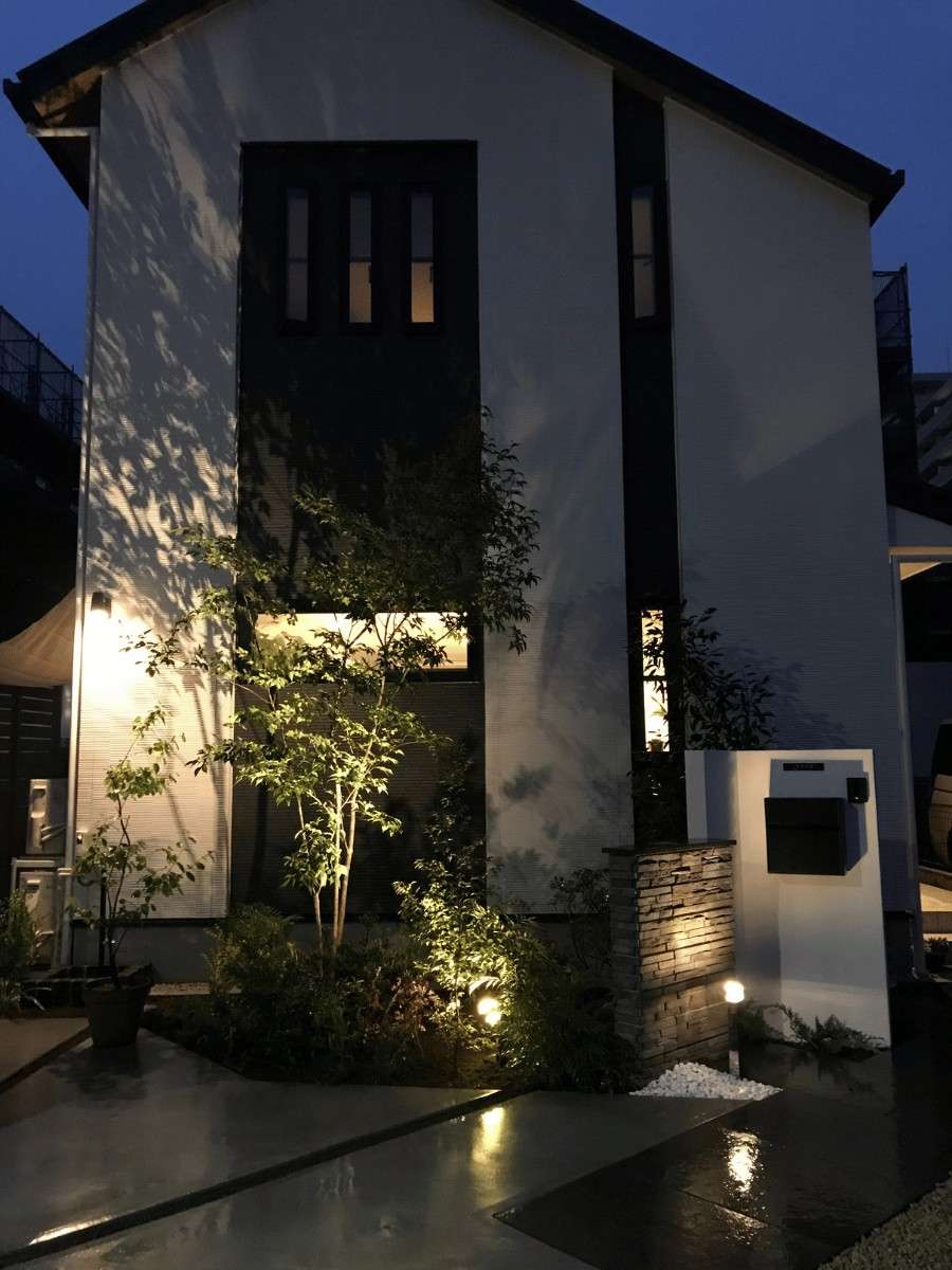 夜間ライトアップされた植栽と門柱。LIXIL美彩の照明が壁面に陰影を映し出す、上質な夜の外構空間。