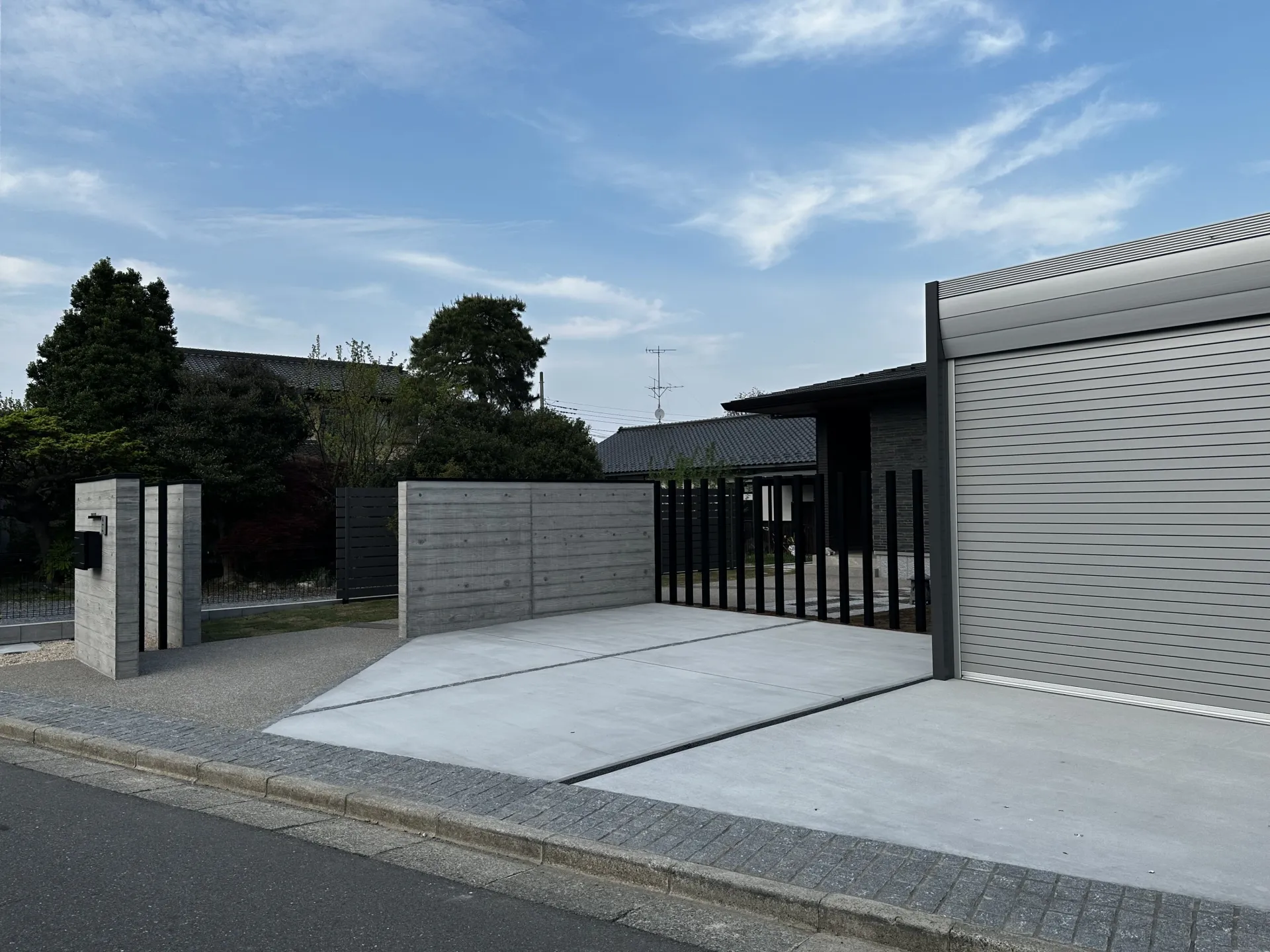 グレーを基調としたモダンデザイン電動シャッターガレージとコンクリート門塀が落ち着いた存在感を放つ