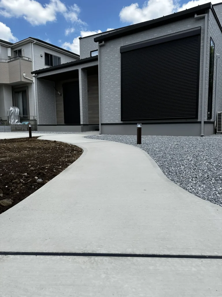 曲線を描くコンクリートアプローチ全景。柔らかな動線が住まいへと自然につながる新井工業の施工事例。