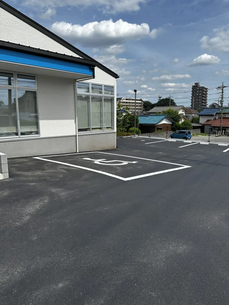 クリニック正面のアスファルト駐車場。視認性の高い白の区画線。障碍者マーク2