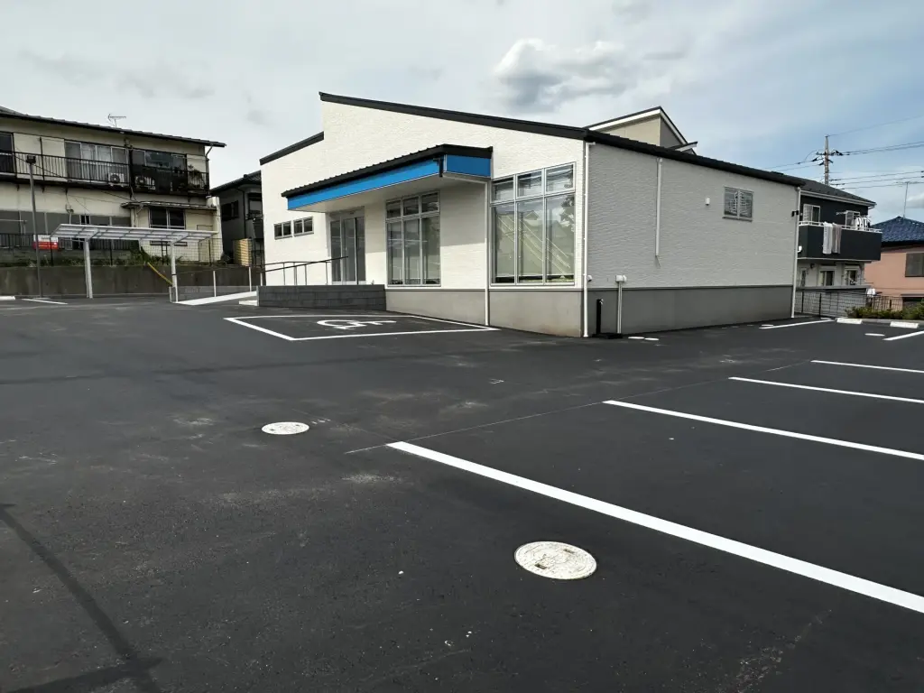 所沢市のクリニック外構。白い建物と調和するアスファルト舗装の駐車場全景